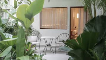 Un espace patio avec une table blanche et deux chaises, entouré d’une végétation luxuriante.