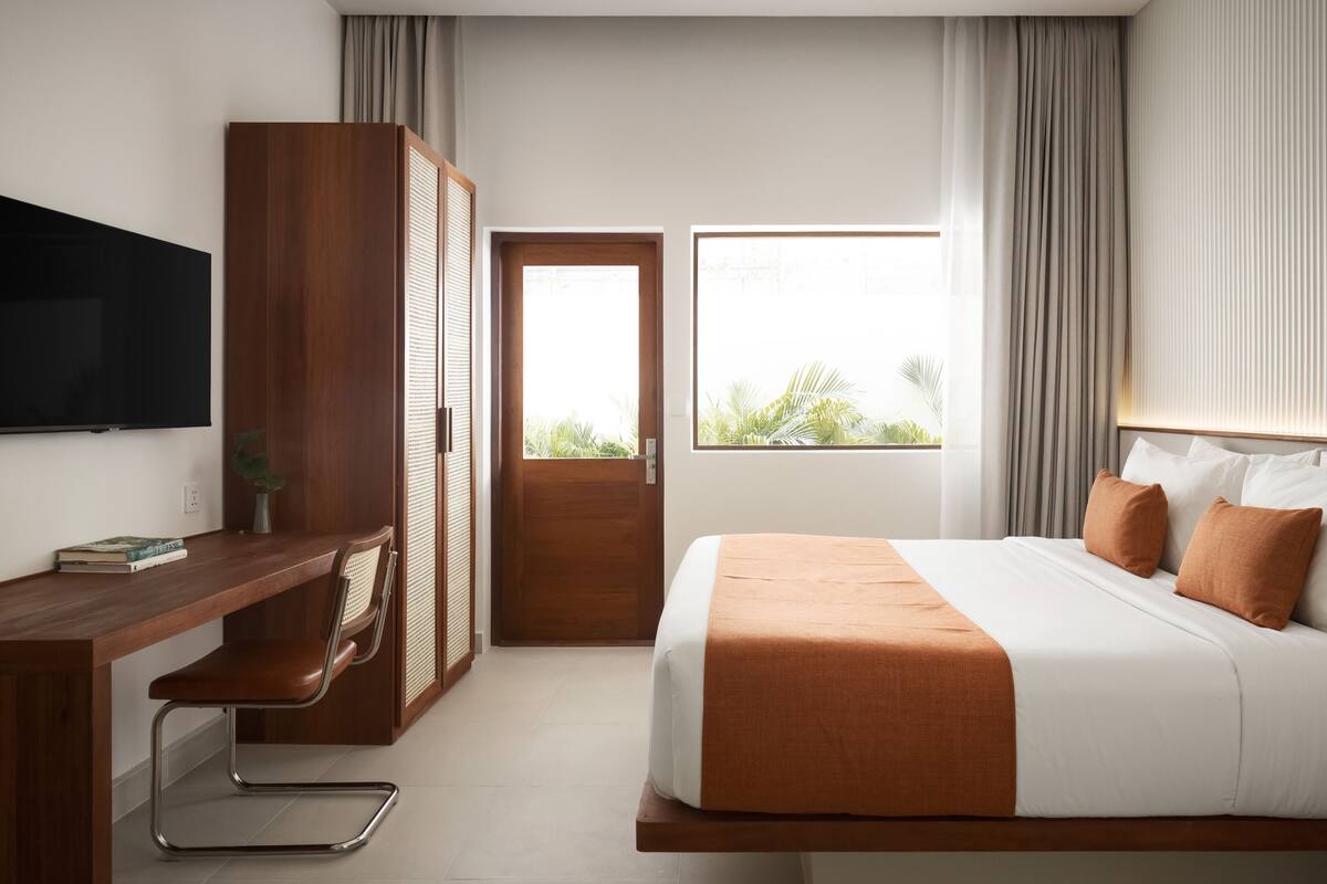 Ein Hotelzimmer mit einem Bett, einem Schreibtisch, einem Fernseher und einem Vorhangfenster.