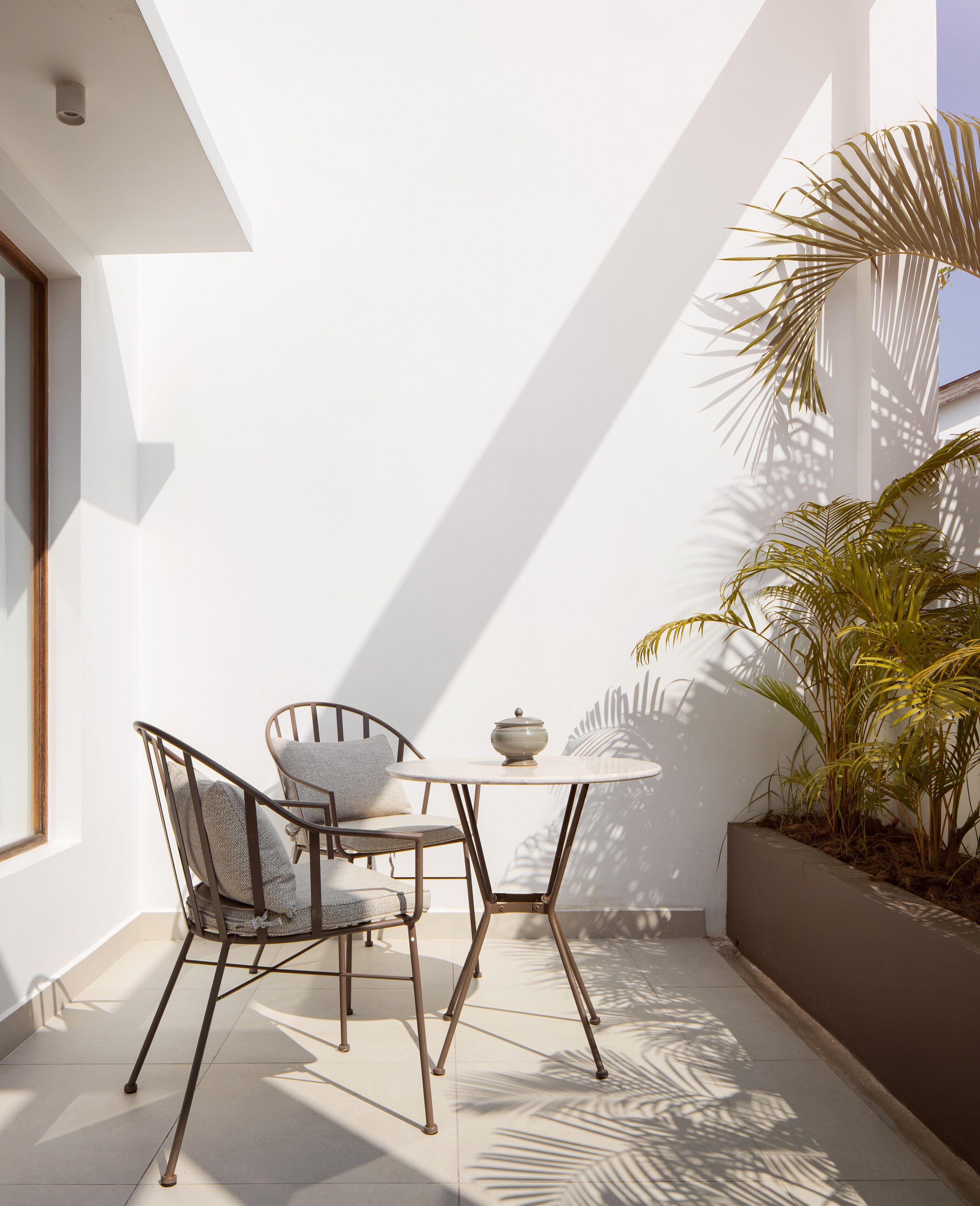Un pequeño espacio al aire libre con una mesa y dos sillas, una planta en maceta y una pared blanca.