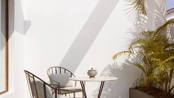 A small outdoor seating area with a table and two chairs, a potted plant, and a white wall.
