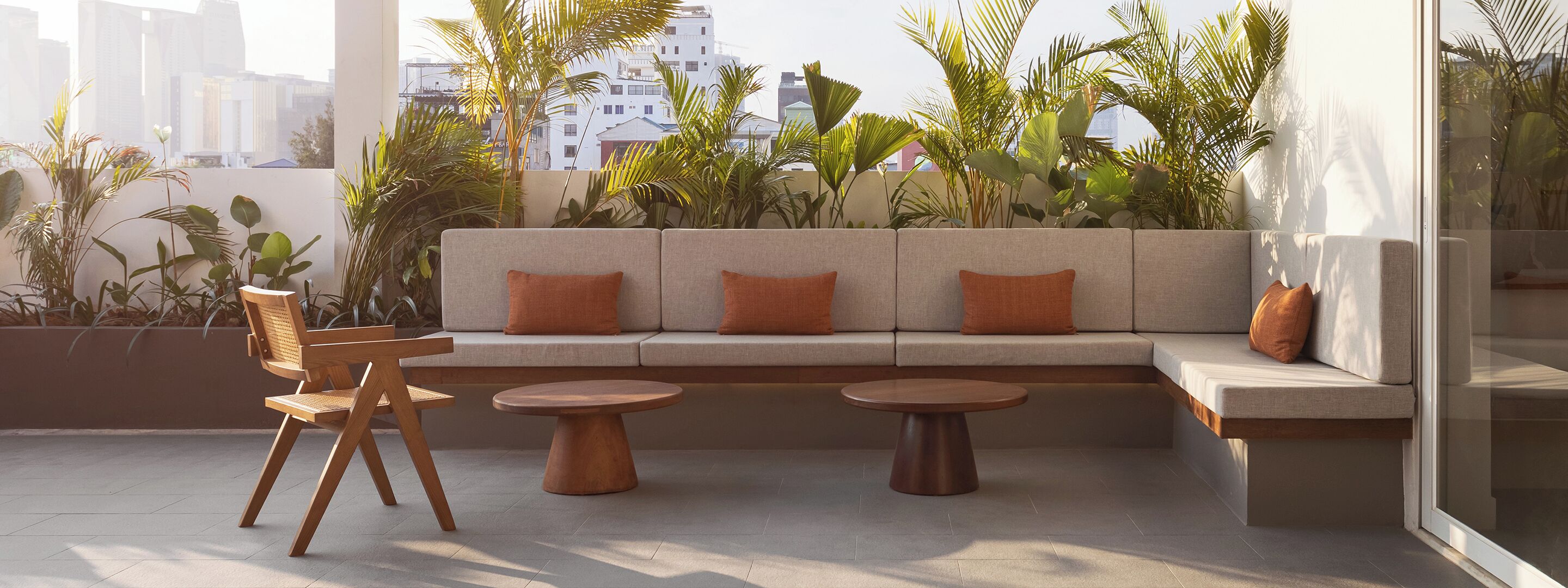 A modern outdoor seating area with a sofa, two round tables, and a wooden chair.