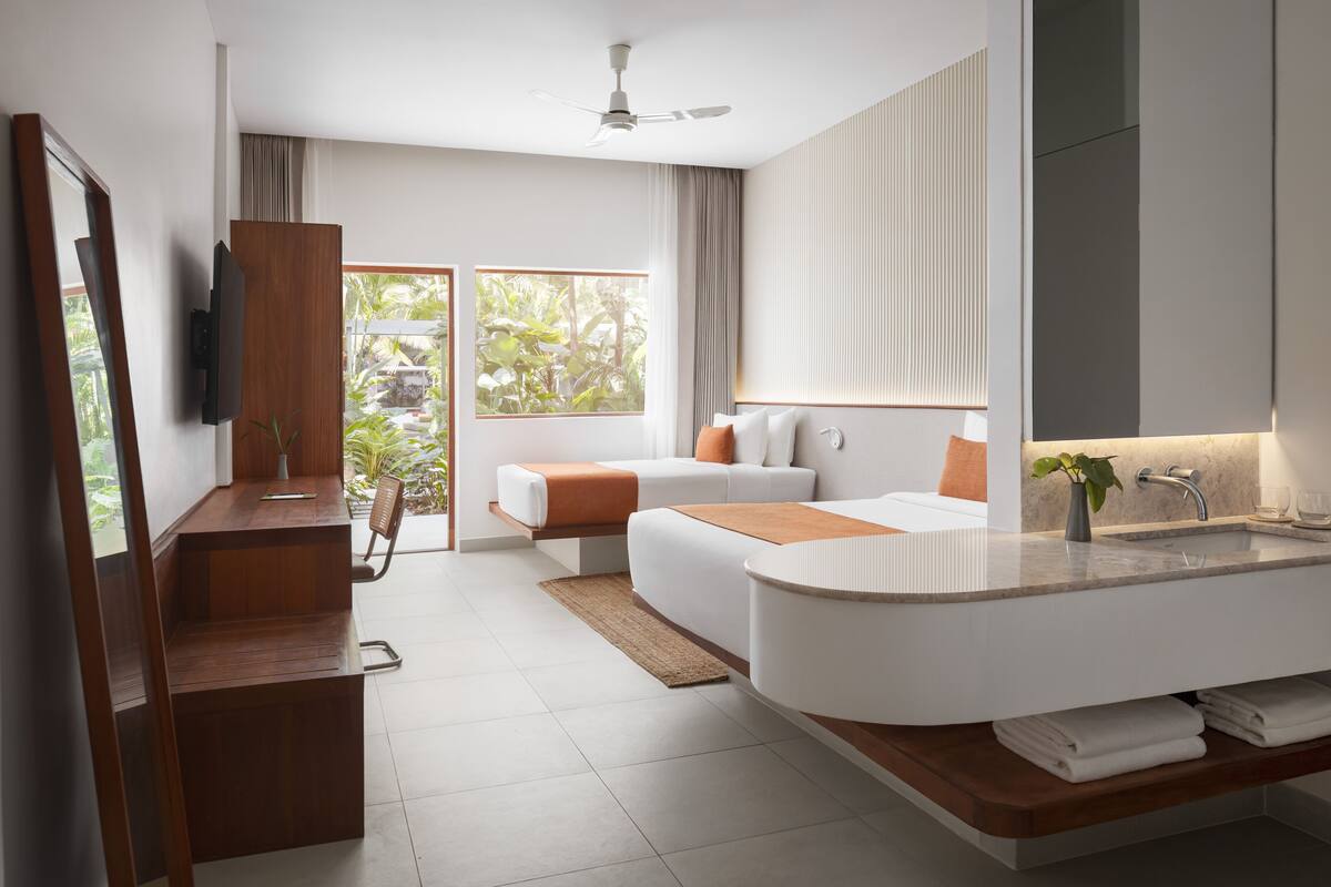 Ein modernes Hotelzimmer mit einer großen, gebogenen Badewanne, einer Schlafsofa, einem Flachbildfernseher und einem großen Fenster mit Blick auf Grünflächen.
