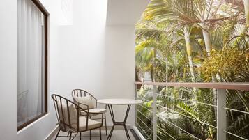 Un balcon avec une petite table et deux chaises, donnant sur un jardin luxuriant où poussent différentes plantes et arbres.