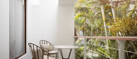A balcony with a small table and two chairs, overlooking a lush garden with various plants and trees.