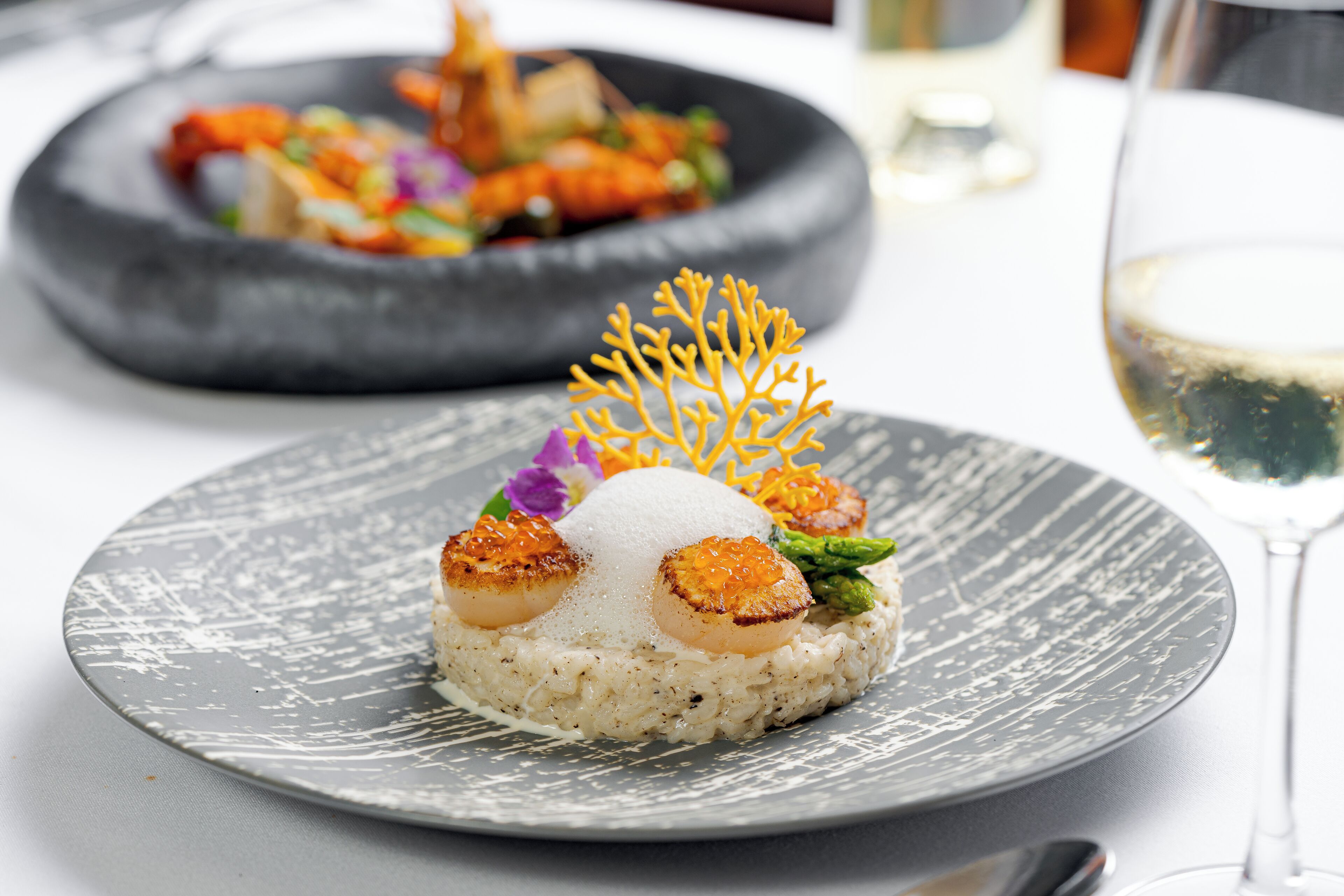 Un plato de comida con vieiras y arroz, adornado con una flor amarilla y una flor púrpura.