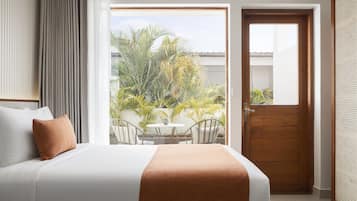 Habitación de hotel con cama, vista a palmeras, puerta de madera y balcón con mesa y sillas.