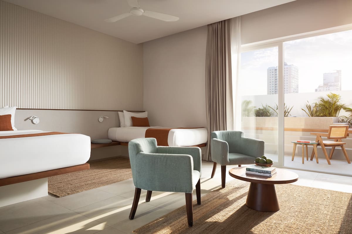 Ein modernes Hotelzimmer mit einem großen Bett, zwei Sesseln, einem Couchtisch und einem Balkon mit Blick auf die Stadt.