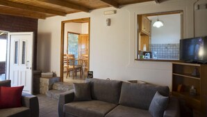 A cozy living room with a sofa, a television, and a kitchen area visible through an open door. - Elia Stavros Villas (Chania)