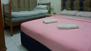 Una habitación con dos camas, una con estructura de madera y la otra con cabecera. Hay una mesita con una botella y una taza.