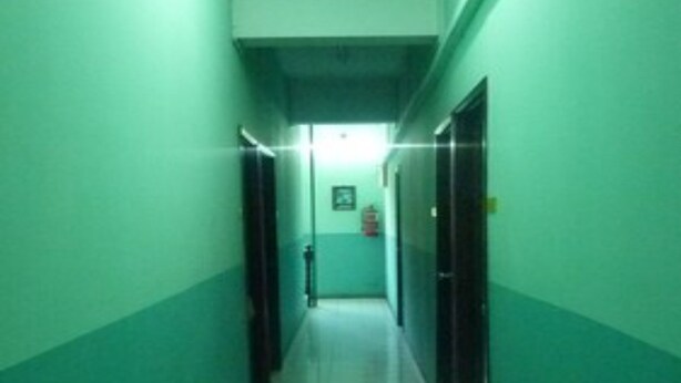 Un pasillo con paredes verdes y pisos de baldosas blancas, que conduce a una puerta al final.
