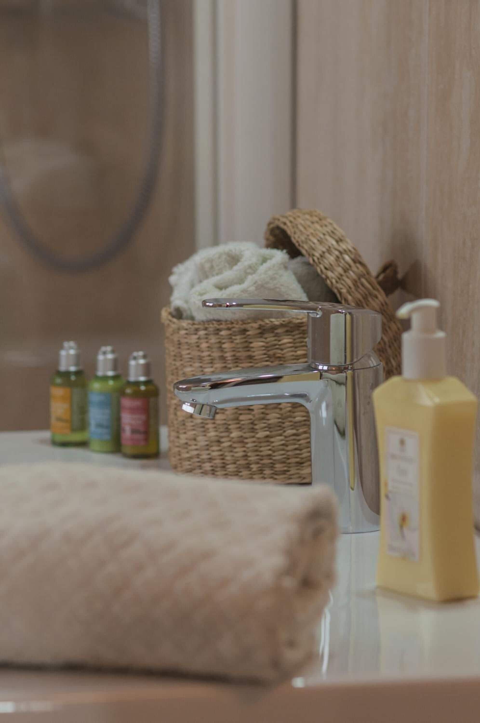 Une salle de bain avec un robinet chromé, un panier en osier contenant une serviette et des flacons de produits de toilette.