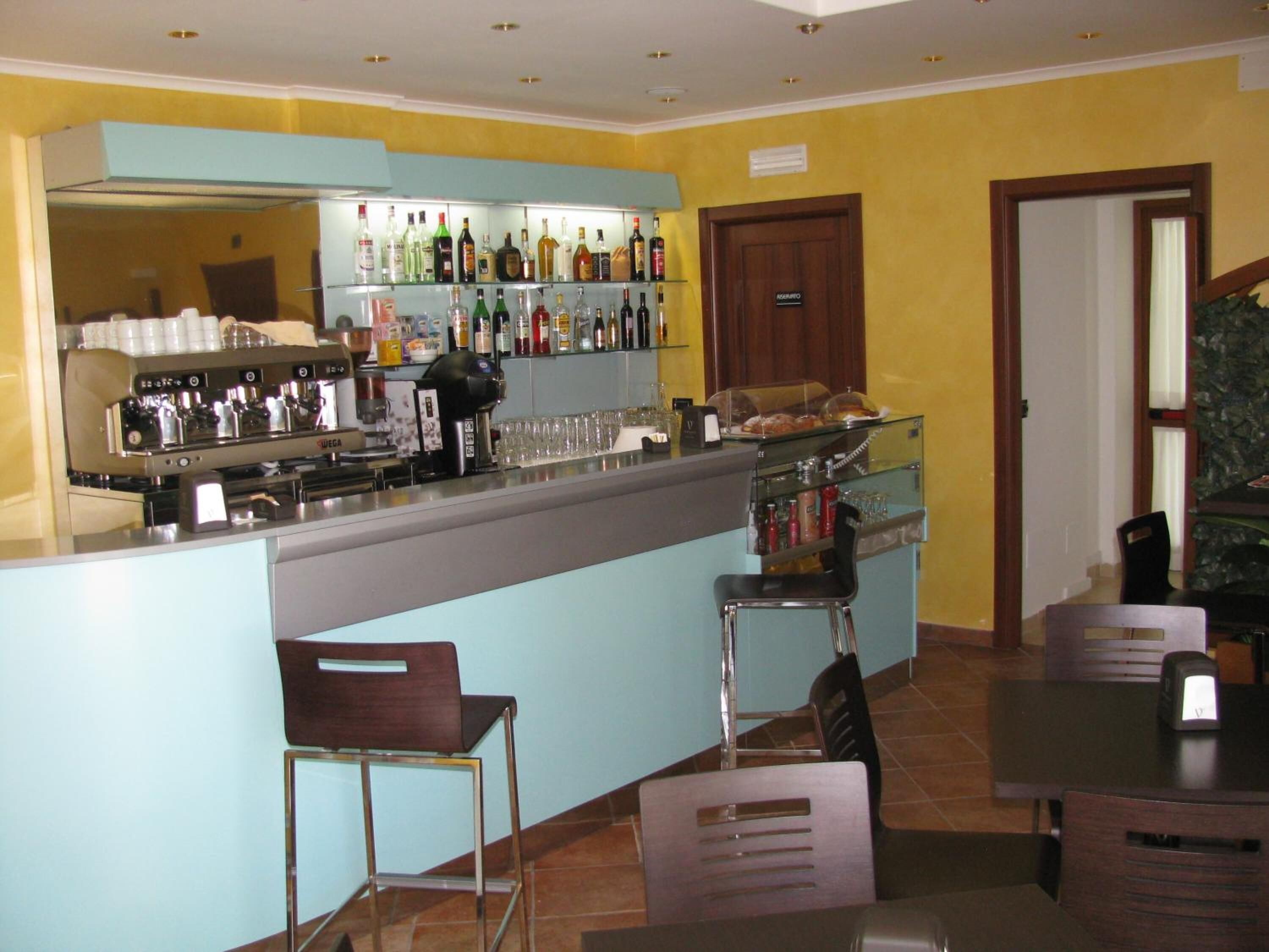 Uma área de bar com balcão, banquetas e diversos tipos de garrafas e copos.