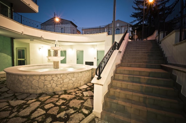 Un patio con una fuente de piedra, una escalera y un edificio con balcones.