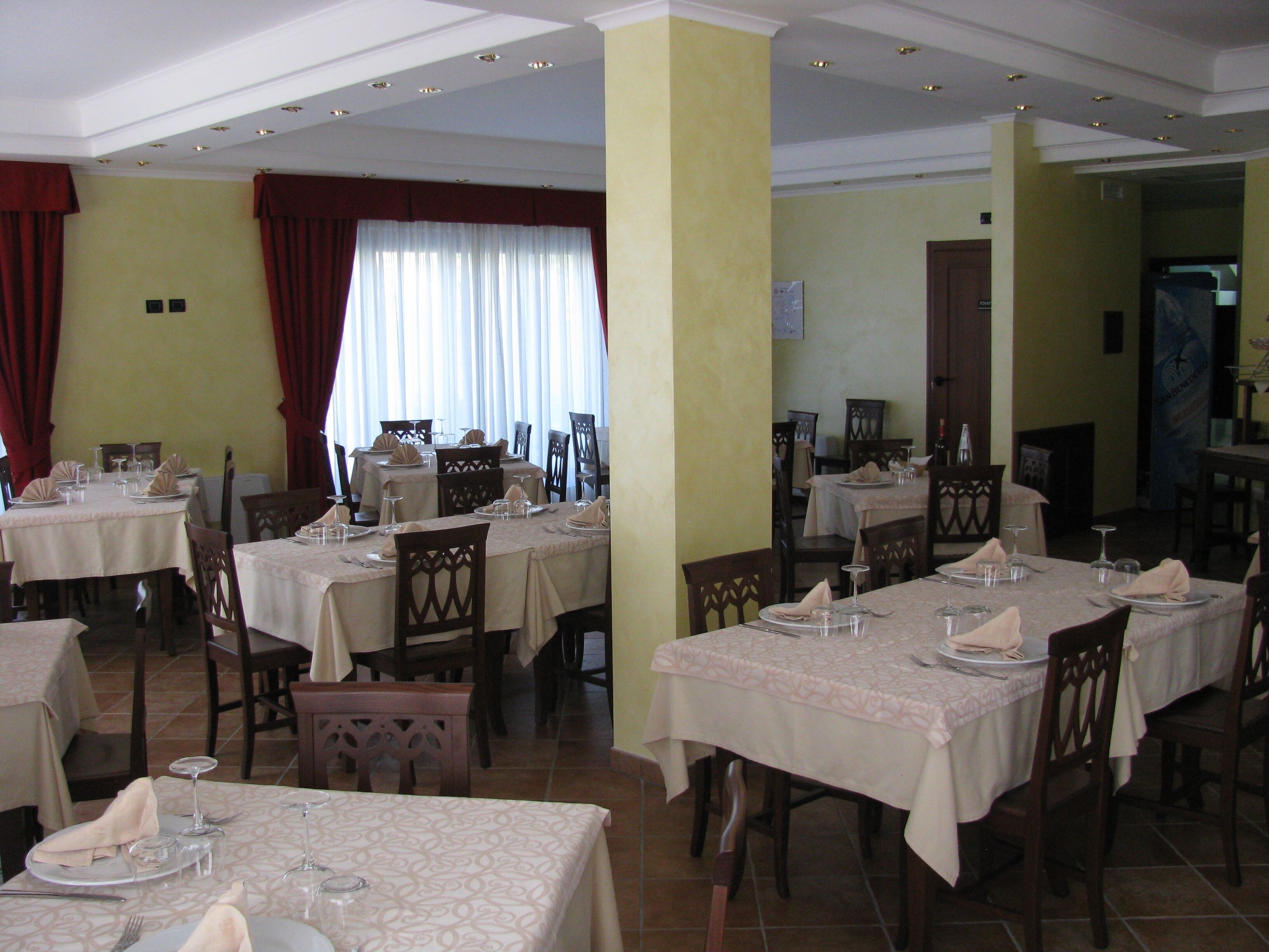Un espace repas avec plusieurs tables dressées pour le service, caractérisé par un motif uniforme sur les nappes et des chaises en bois.