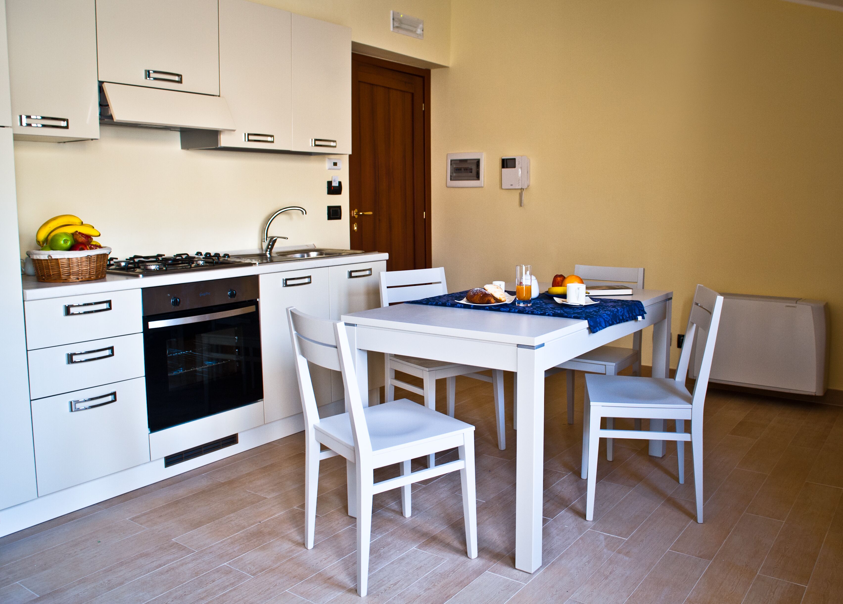 A compact kitchen with white cabinets, a stove, and an oven. There is a dining table with chairs and a blue tablecloth.