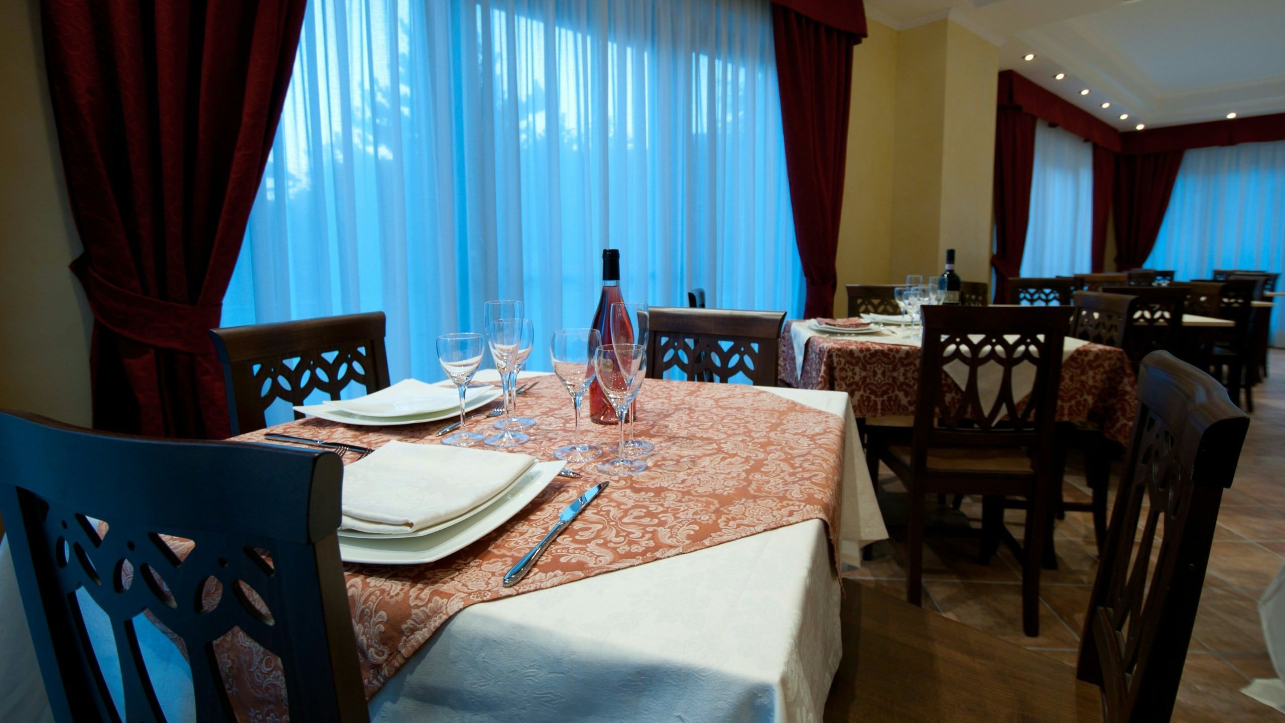 Comedor con mesas dispuestas para dos, con manteles estampados y sillas de madera.
