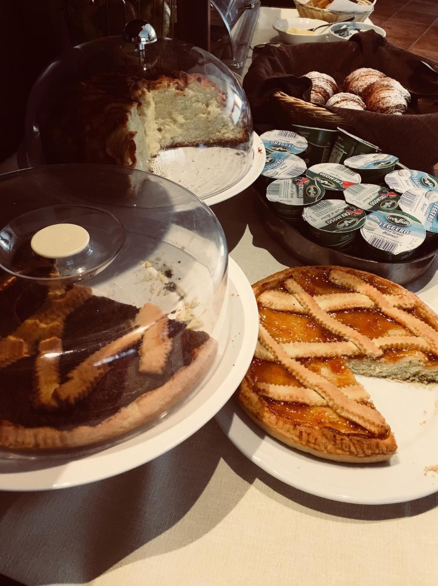 A table with a covered cake, a pie, and a tray of pastries.