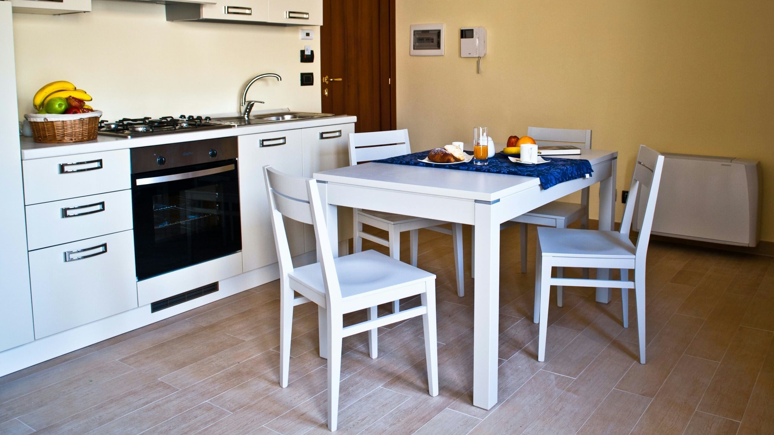 A compact kitchen with white cabinetry, a gas stove, an oven, and a dining table with chairs.