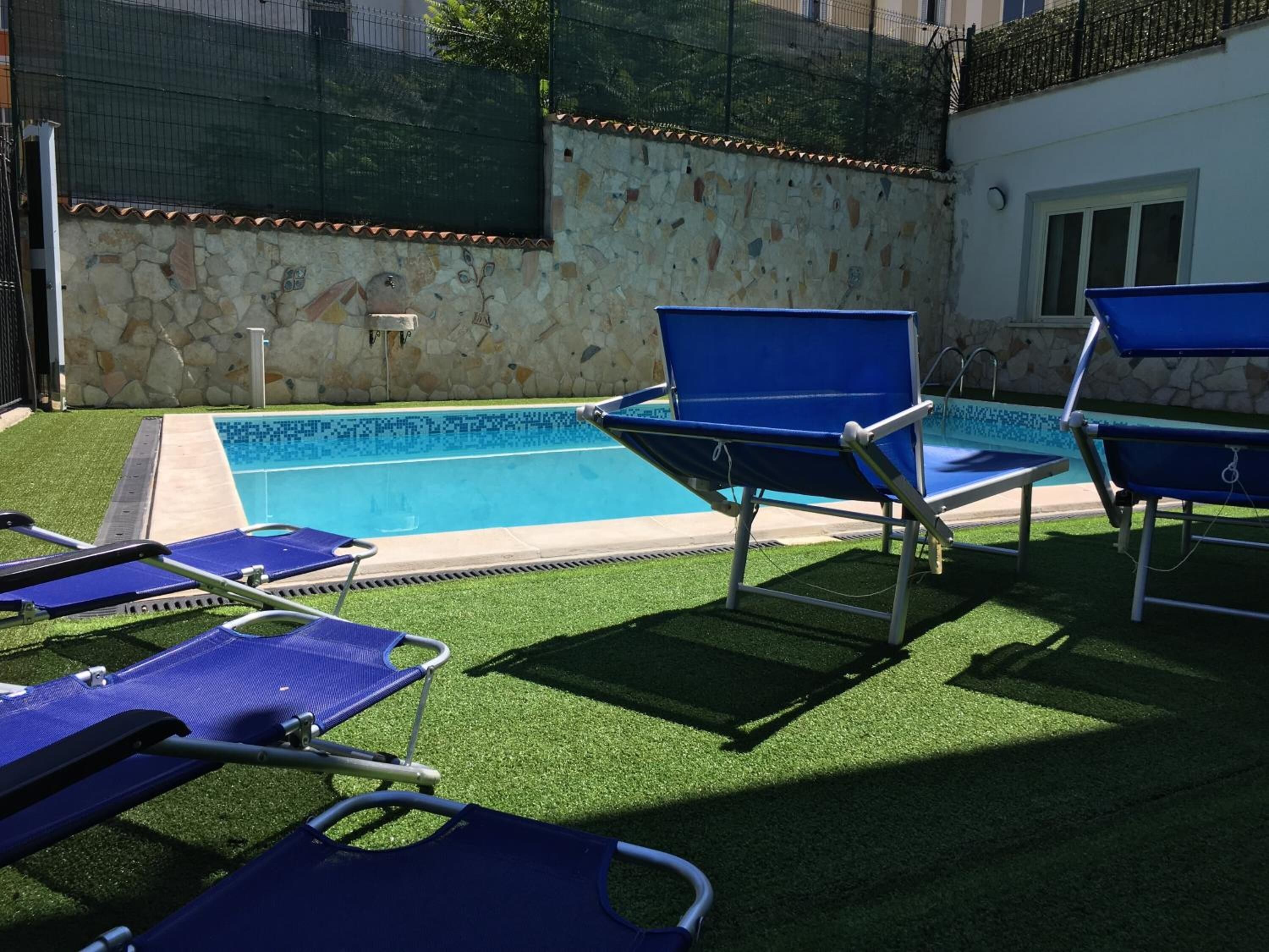Una piscina con sillones reclinables azules y césped artificial.