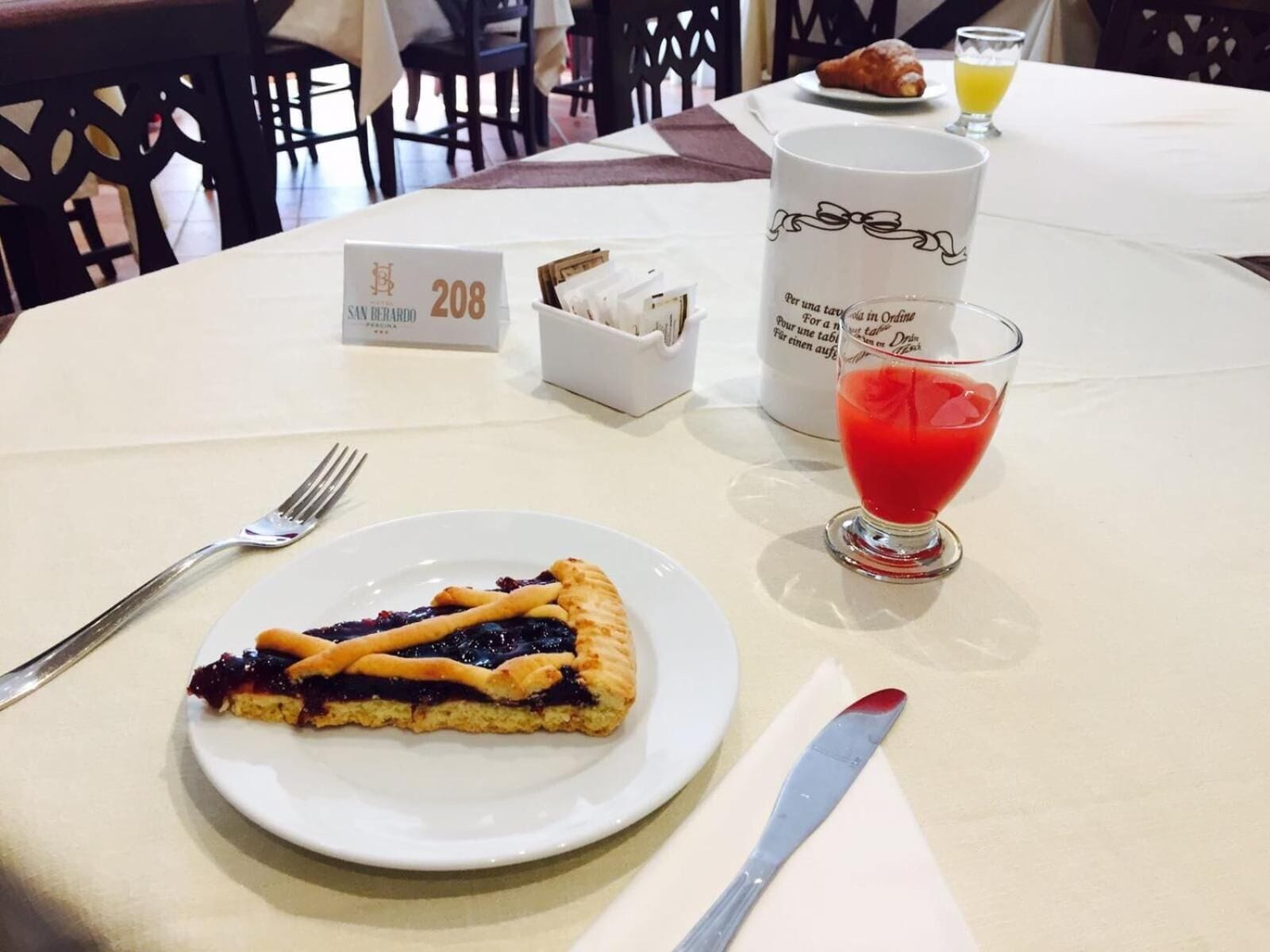 A table with a slice of pie, a glass of red drink, a white mug, and a small box of napkins.