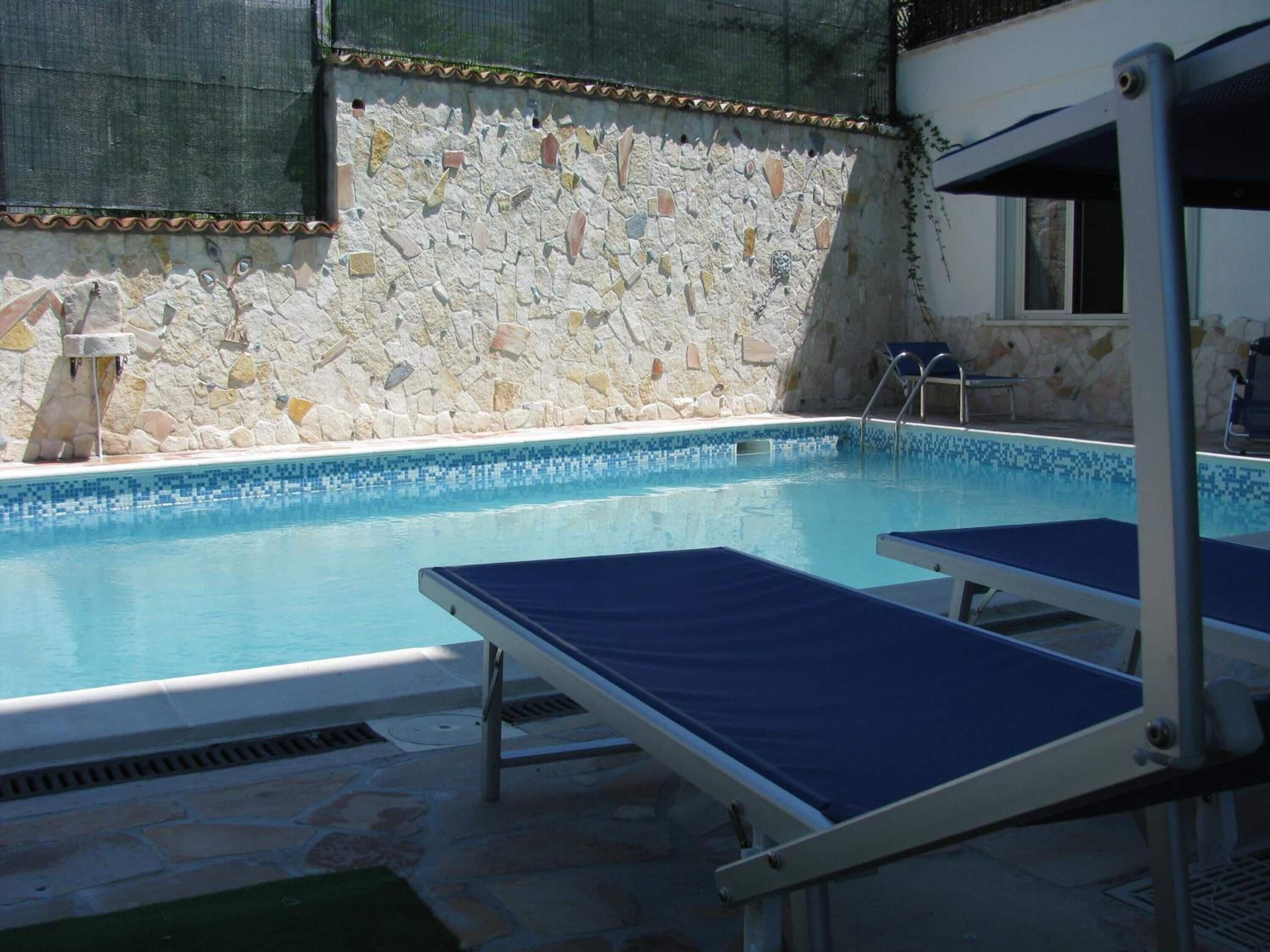 A swimming pool with stone walls and a tiled edge, surrounded by lounge chairs.