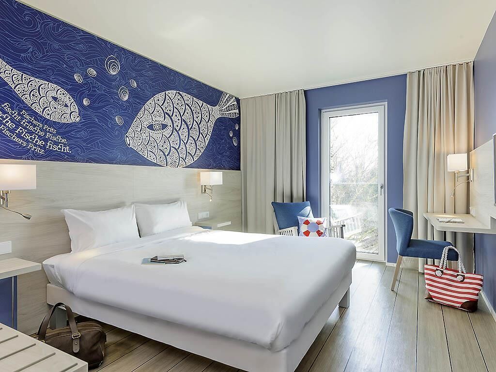 A hotel room with a large bed, a desk, a chair, and a view of the outdoors.
