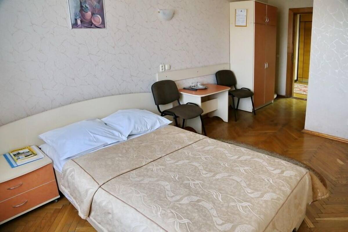 Habitación de hotel con cama, escritorio, dos sillas, armario y una mesita con un libro.