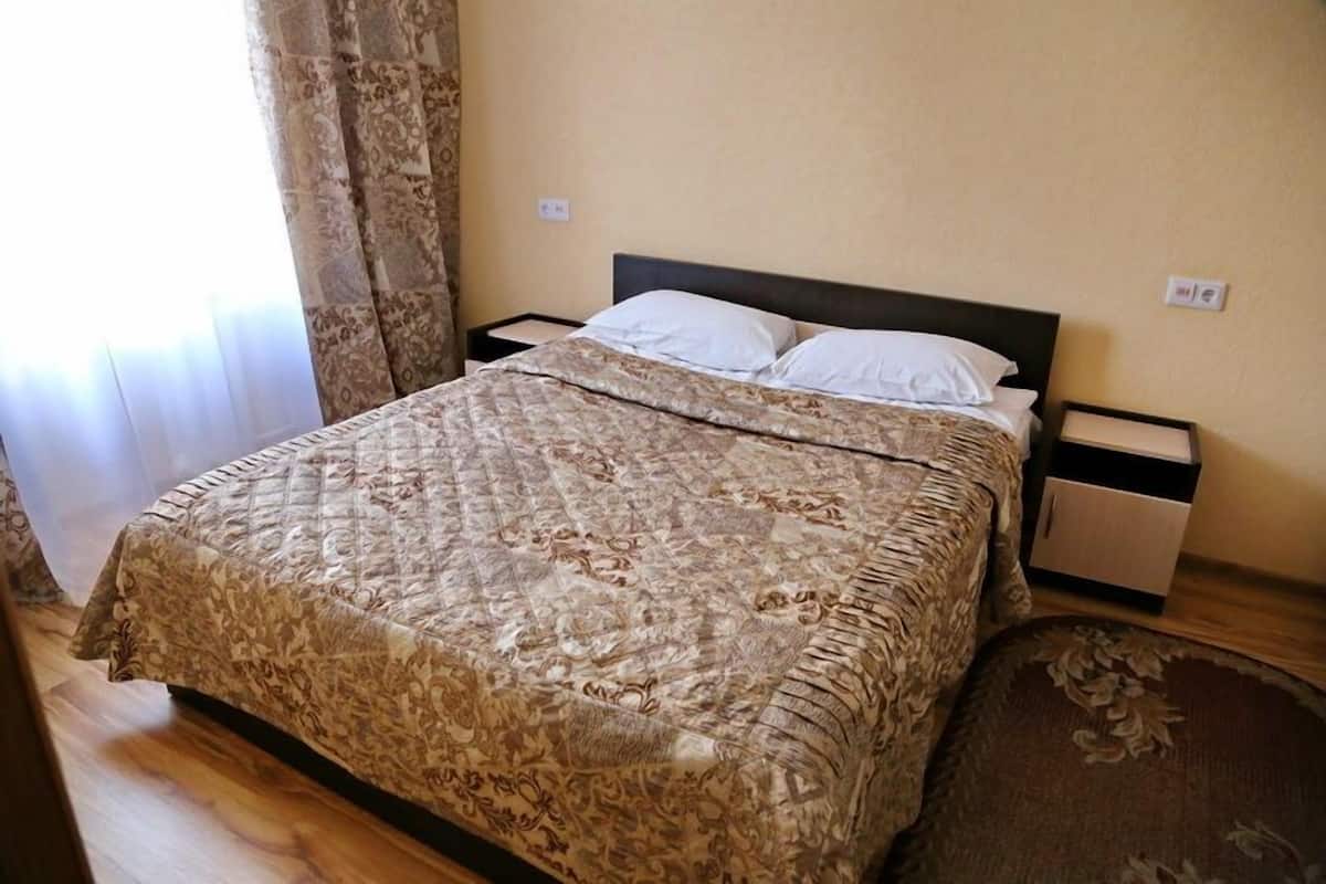 Una cama con una colcha estampada, una mesita de noche y una mesita auxiliar.