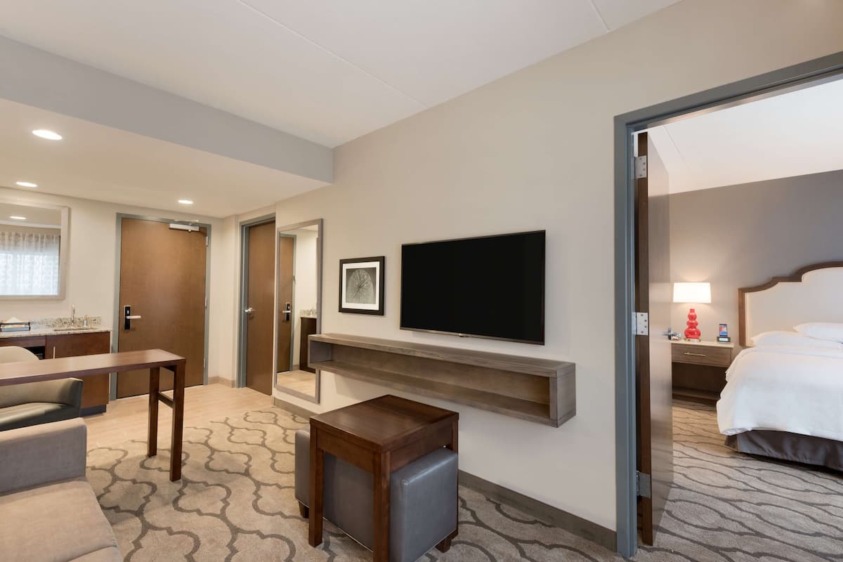 A hotel room with a bed, a TV mounted on the wall, a small table, and a seating area with a sofa and chairs.