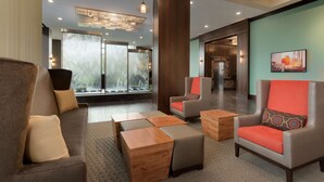 A modern lobby with a sofa, armchairs, wooden ottomans, and a large window with a view. - Embassy Suites by Hilton Chicago Naperville (Naperville)