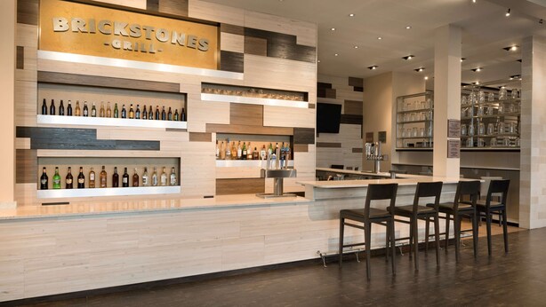 A brickstone grill bar with a wooden and metal decor, shelves with bottles, and a bar counter with chairs. - Embassy Suites by Hilton Chicago Naperville (Naperville)