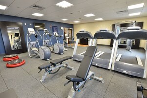 Un gimnasio con diversos equipos de ejercicio, incluyendo cintas de correr, elípticas y bancos de pesas.