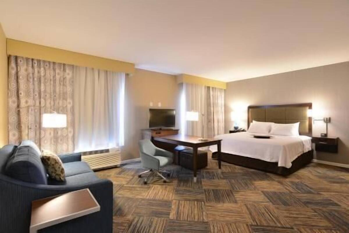 A hotel room with a bed, a desk, a chair, and a sofa.