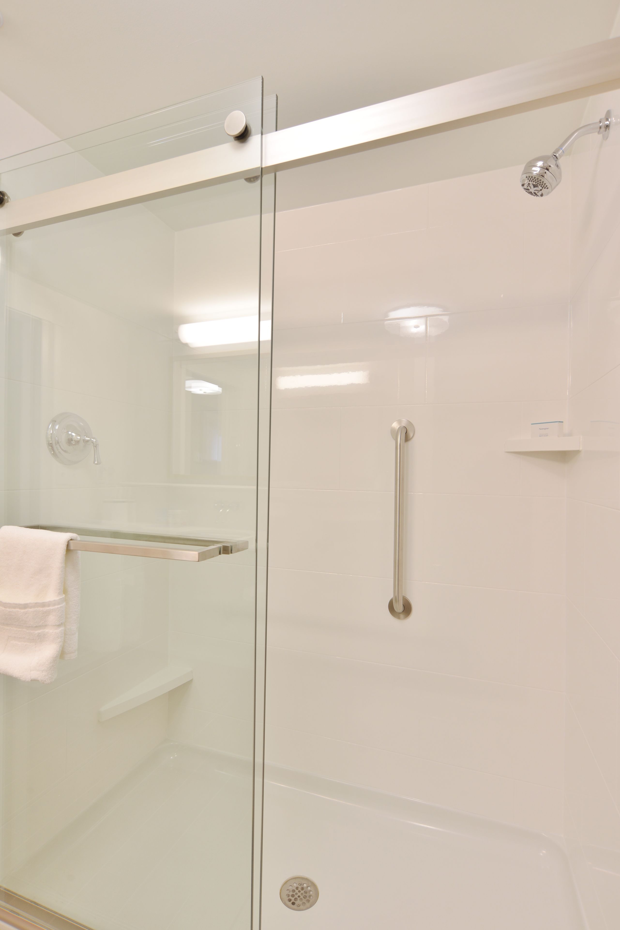 A glass-enclosed shower stall with a glass door, a towel rack, and a handheld showerhead.