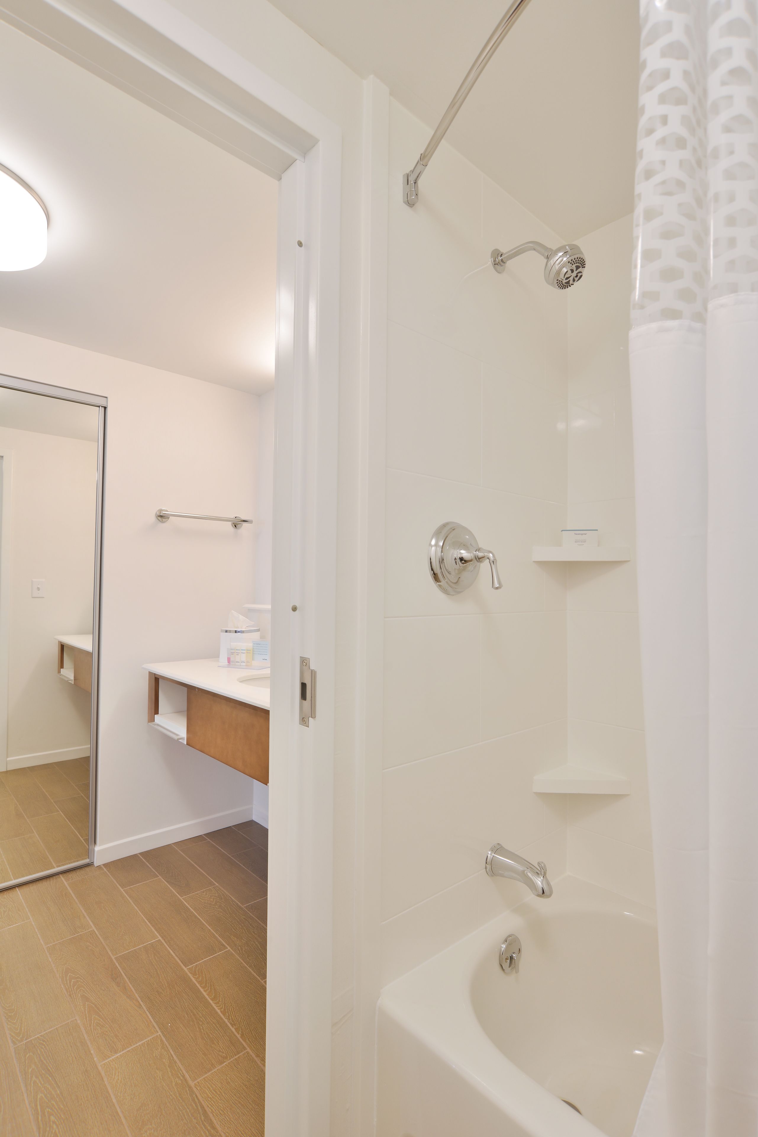 A modern bathroom with a bathtub, shower, and a mirror.