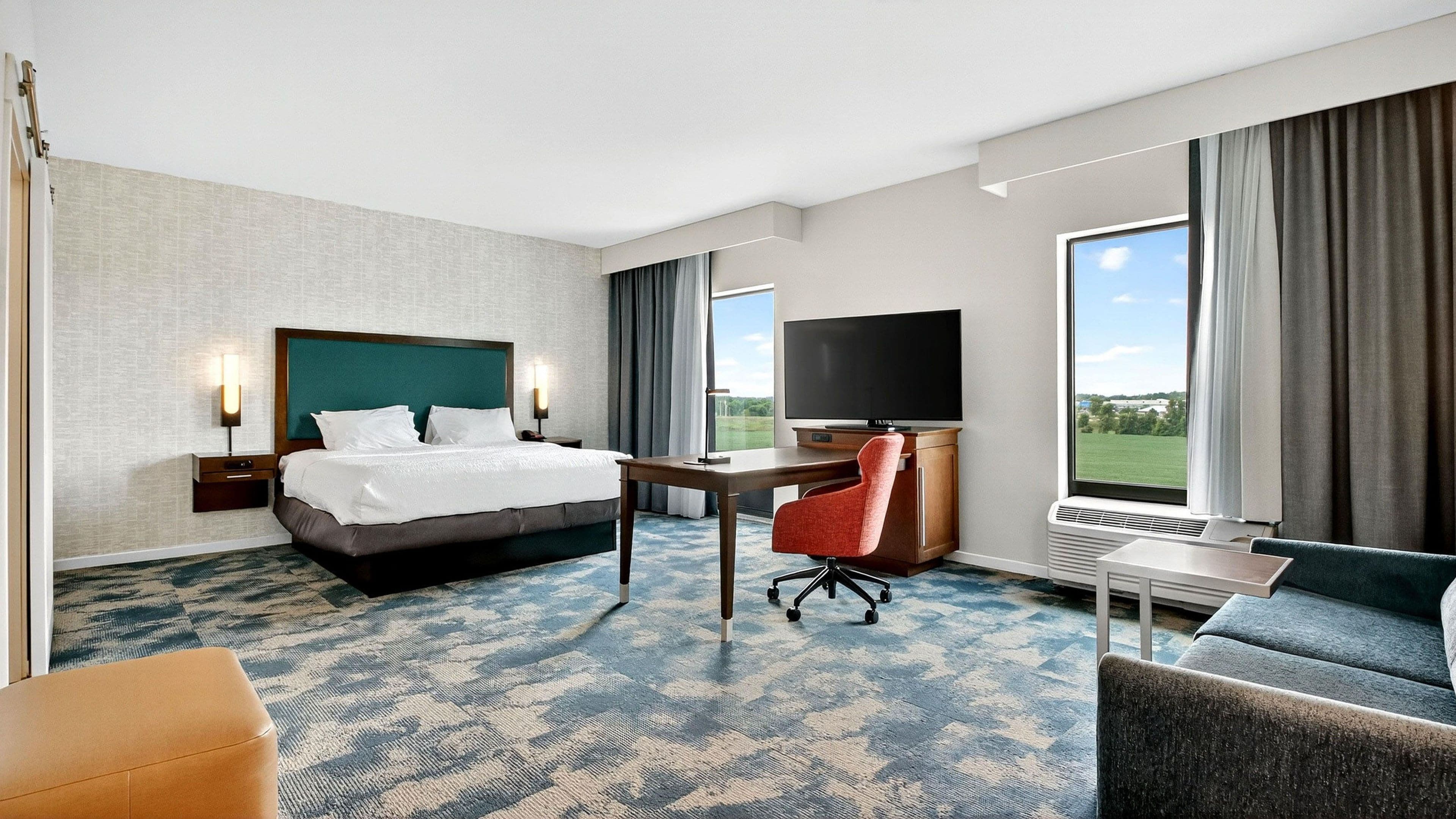 Quarto de hotel com cama, escrivaninha, televisão e vista para o exterior.