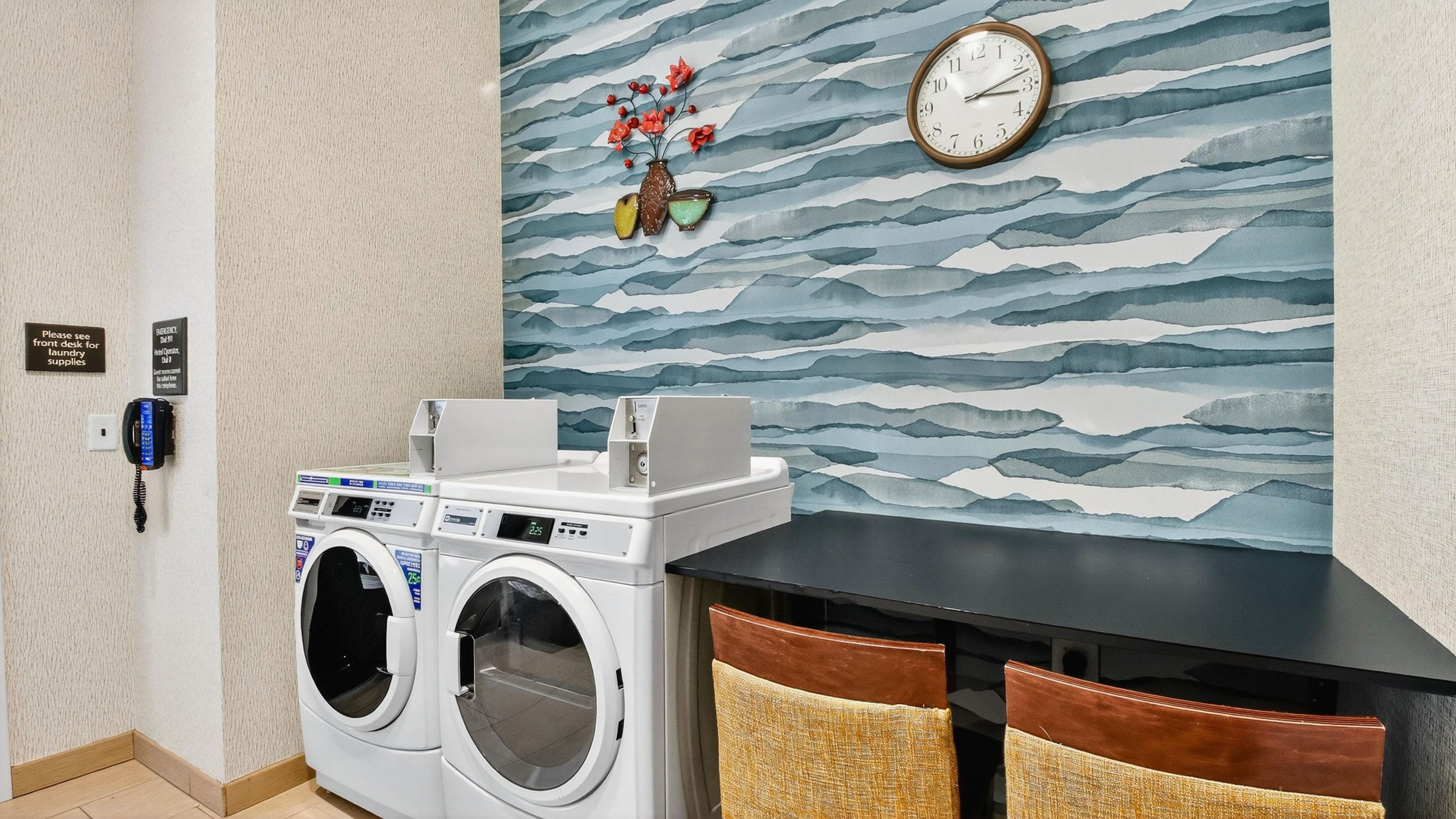 A laundry room with two front-loading washing machines, a wall-mounted clock, and a decorative wall with a wave pattern.
