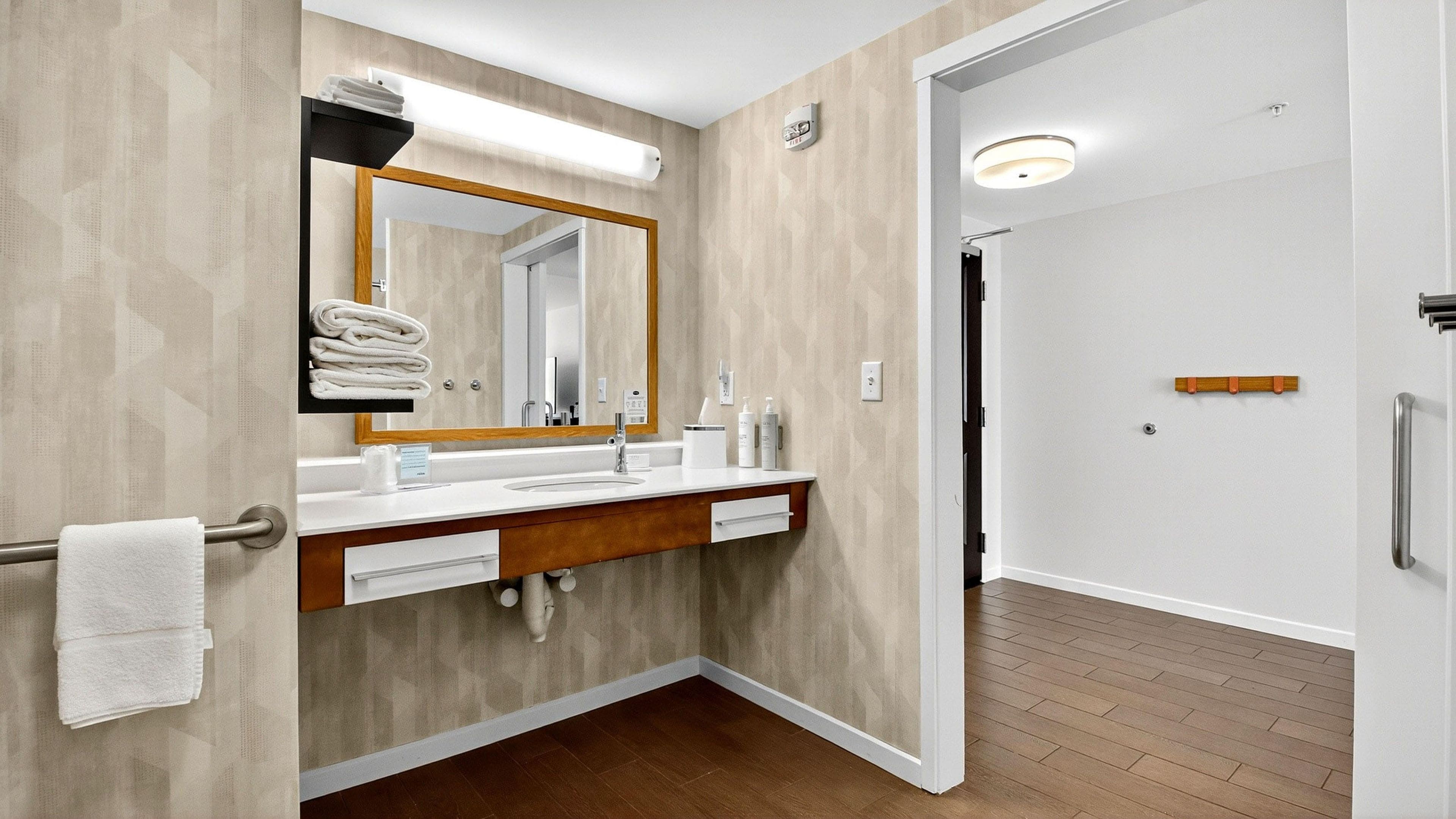 A modern bathroom with a wooden vanity, a large mirror, and a walk-in shower.