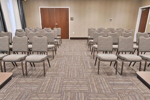 Un salón de conferencias con hileras de sillas, piso alfombrado y una puerta de madera.