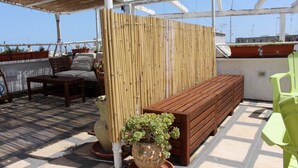 A rooftop terrace with a wooden bench, a bamboo partition, and potted plants. - B&B Casa Cimino (Monopoli)