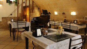 A rustic dining area with stone walls, wooden tables, and chairs. There are multiple tables set with plates, glasses, and cutlery. A bread machine is visible on one table. - B&B Casa Cimino (Monopoli)