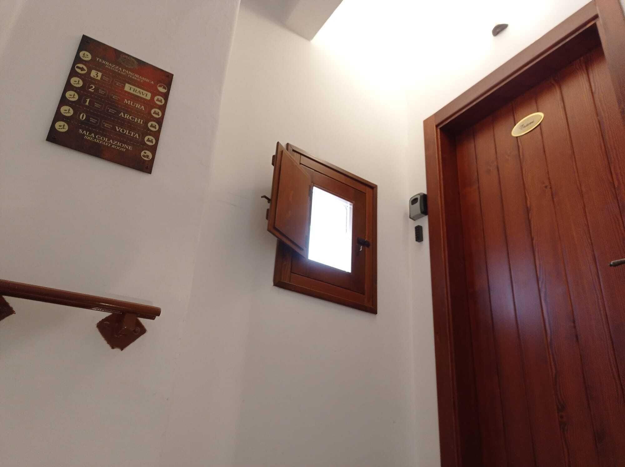 Une porte en bois avec une petite fenêtre, une plaque fixée au mur indiquant les noms des pièces, et une main courante en bois.
