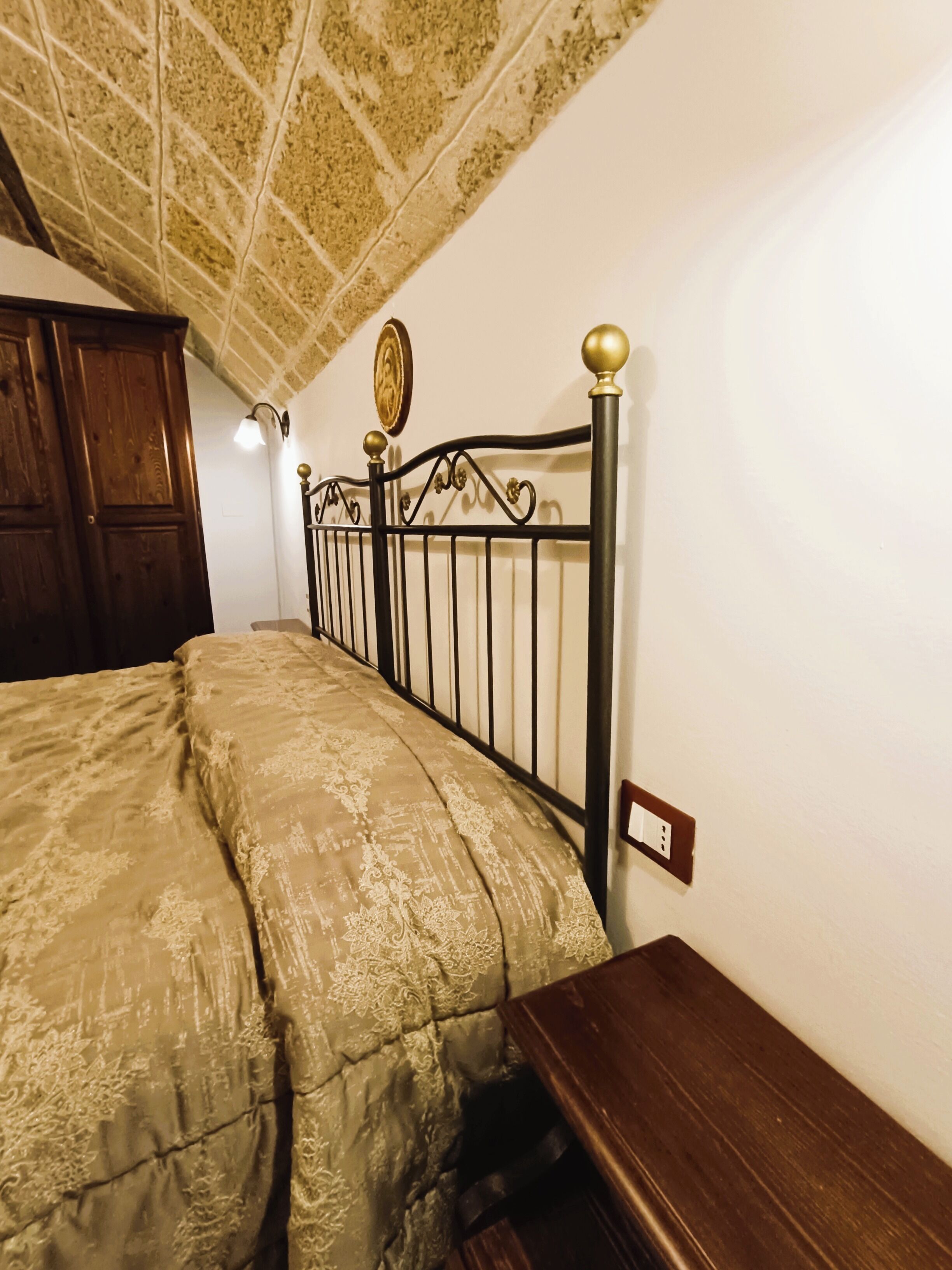 A bedroom with a bed, a wooden wardrobe, a wall-mounted light fixture, and a decorative plate.