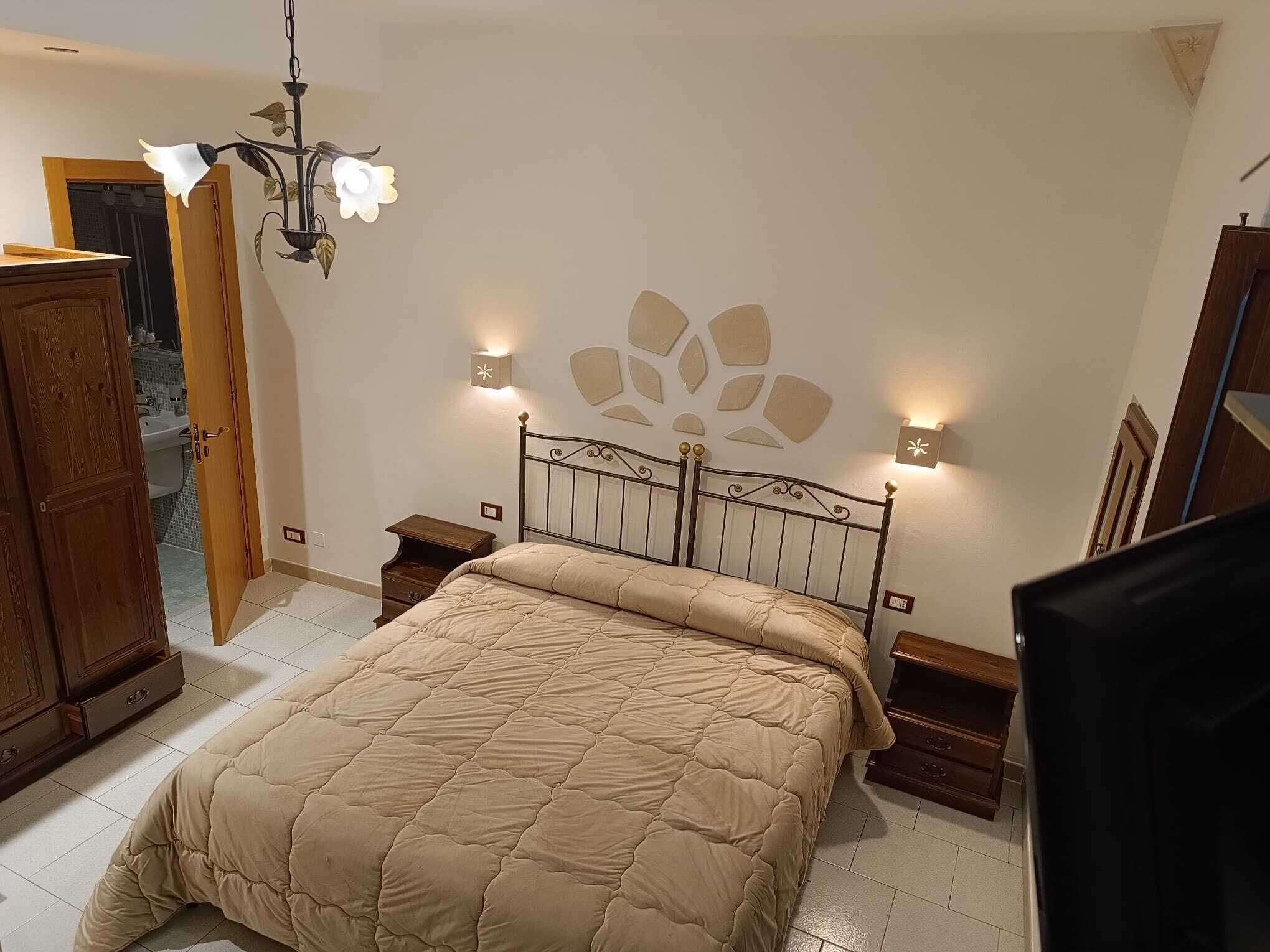 Une chambre à coucher avec un lit, des tables de chevet en bois, une commode, un lustre et des appliques murales.