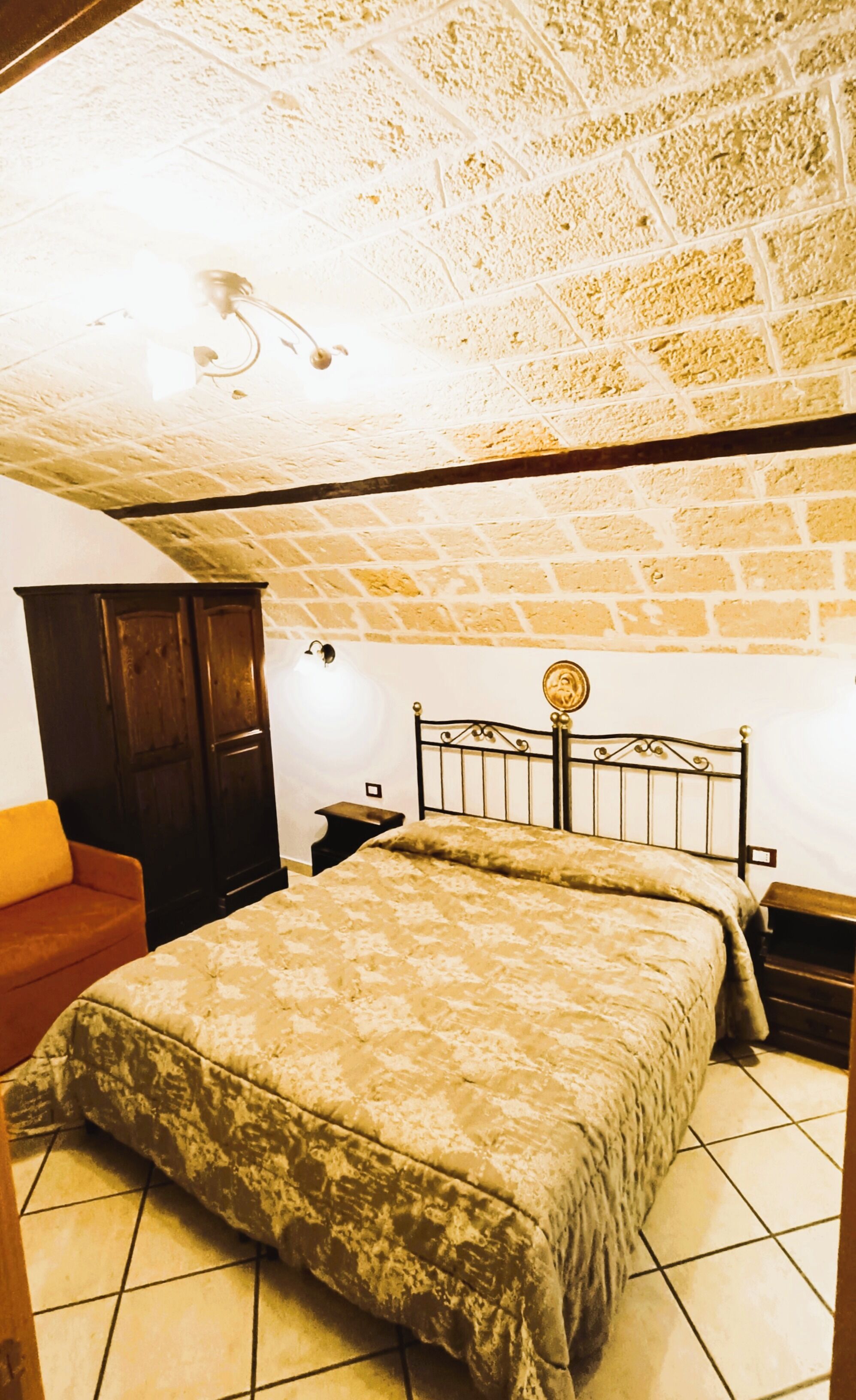 A bedroom with a brick ceiling, a bed with a headboard, a wooden wardrobe, and a red sofa.