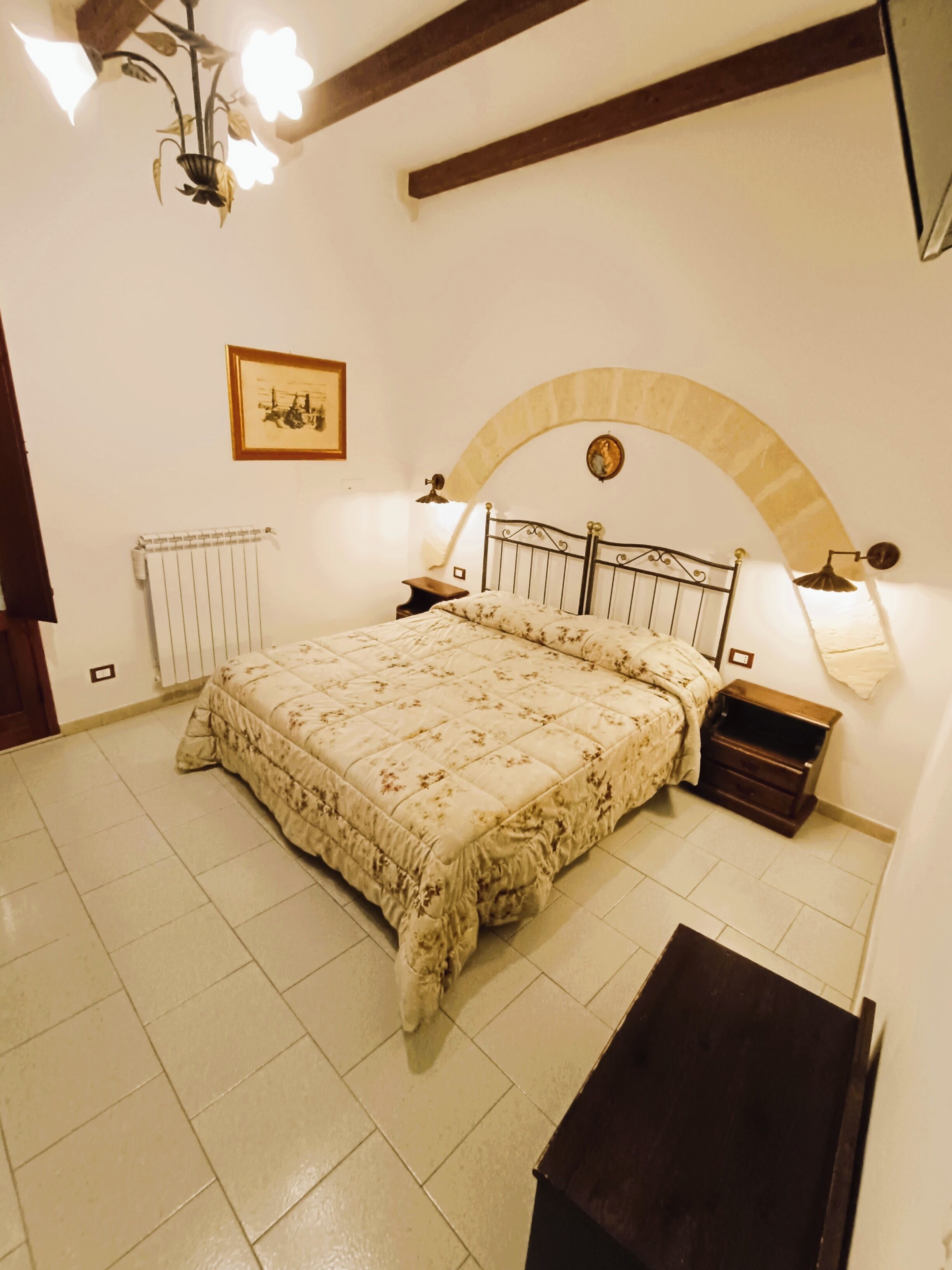 A bedroom with a bed, a nightstand, a lamp, a radiator, and a picture on the wall.