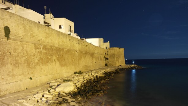 A coastal stone wall with buildings on top, overlooking a calm sea at night. - B&B Casa Cimino (Monopoli)