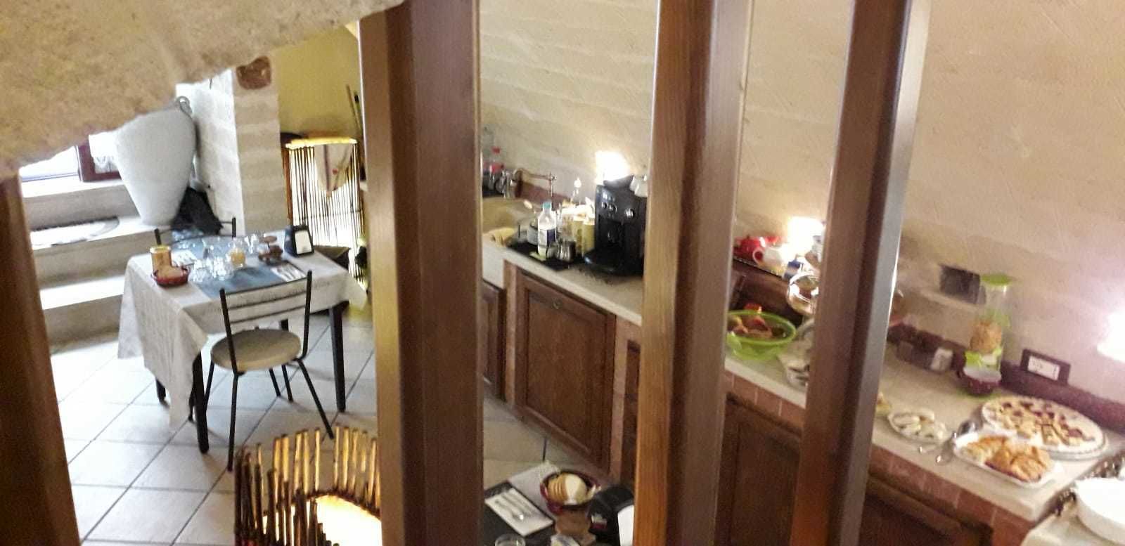 A dining area with a table set for two, a kitchen area with various appliances and food items, and a view of the outdoors.