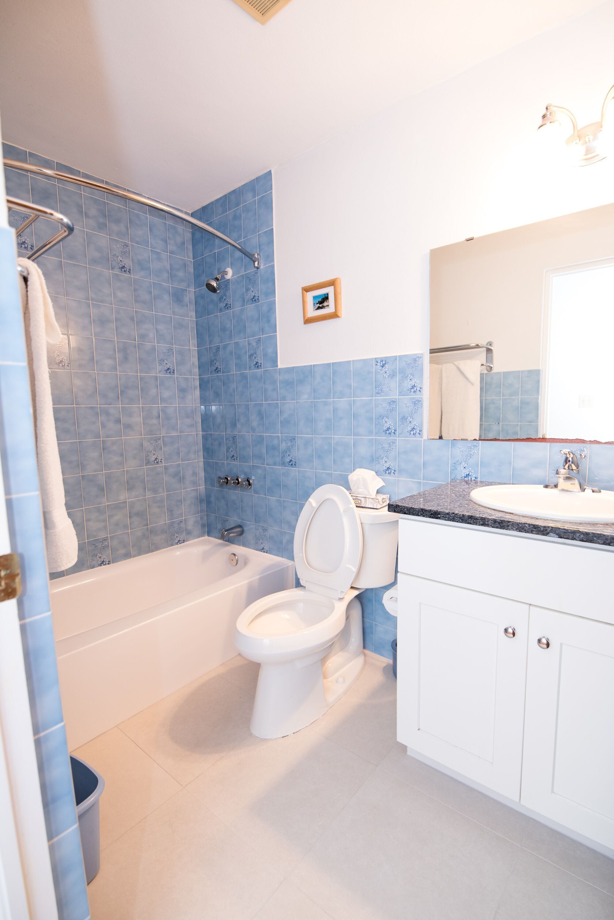 A bathroom with a bathtub, toilet, and sink, featuring blue tiles and white fixtures.