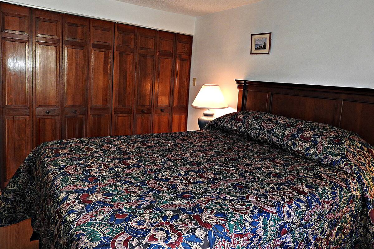 A bedroom with a large bed, wooden wardrobe, and a nightstand with a lamp.